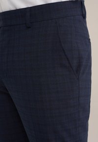 Pantalon sur mesure bleu marine en tissu texturé, avec un motif à carreaux, des poches latérales et une taille lisse.