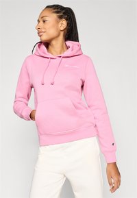 Ροζ φούτερ με κουκούλα, κορδόνια και τσέπη μπροστά. Διαθέτει κεντημένο λογότυπο στο στήθος και λεπτομέρεια με λογότυπο στο μανίκι.