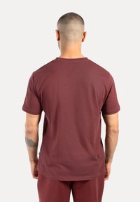 Maglietta a maniche corte color bordeaux con scollatura a girocollo classica. Texture liscia con vestibilità comoda, mostrata dal retro, senza ulteriori dettagli visibili.