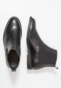 Bottines Chelsea en cuir noir avec des panneaux latéraux élastiques, une finition lisse et une languette au talon. Semelle en caoutchouc plate avec des détails de couture.