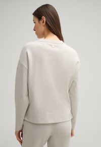 Light grey cotton sweatshirt with a relaxed fit, round neckline, and a small logo detail on the back. Soft texture, long sleeves.