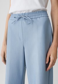 Pantalons larges bleu clair en tissu texturé, avec taille élastique et cordon de serrage. Comprend des poches latérales et une coupe décontractée.
