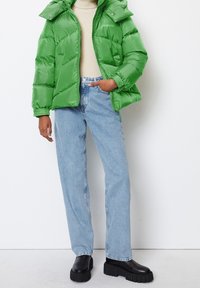 Bright green puffer jacket with a high collar, ribbed cuffs, and front zipper. Paired with light blue jeans and black chunky boots.