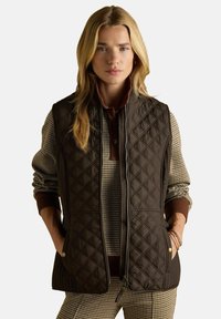 Browna, kvadrāta raksta vestes ar dimanta modeli, ar rāvējslēdzēju priekšpusē, divām sānu kabatām un apkakli, pārvalkot šaha raksta džemperi.