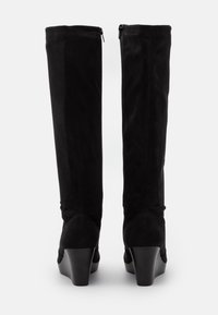 Bottes hautes jusqu'au genou en daim noir avec un talon compensé effilé et des fermetures éclair latérales. Texture lisse, design ajusté, et détails de couture subtils.