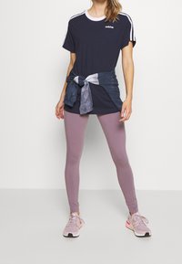 Camiseta azul marino con rayas blancas, combinada con leggings lila. Camiseta de tie-dye atada en la cintura, complementada con zapatillas rosas claras.