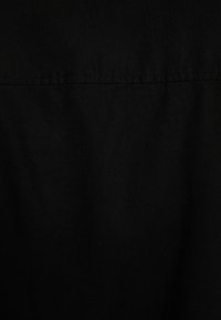 Black fabric background with visible horizontal seam stitching near the top, showing slight texture and drape.