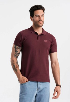 Polo bordeaux avec un col, des manches courtes et un petit emblème sur la poitrine ; associé à un jean bleu clair. Matière en coton texturé.