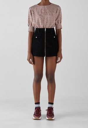 Person iført en ternet bluse med albuelange ærmer, en sort fløjlsmini nederdel med lynlås foran, stribede sokker og bordeaux sneakers.