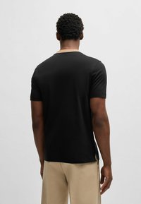 T-shirt nera a maniche corte con scollatura rotonda e slit laterali, realizzata in tessuto liscio, mostrata dal retro.