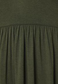 Tissu de robe vert olive avec un haut ajusté et une texture froncée à la taille, créant une jupe fluide. Mélange de coton doux et léger.