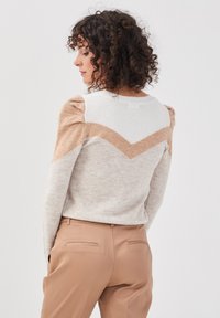 Suéter de punto con un patrón en forma de Chevron, que presenta colores beige, marrón claro y crema; mangas texturizadas y cuello redondo.
