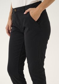 Pantaloni neri con una texture liscia, dotati di tasche laterali, chiusura con bottone in vita e un design slim fit.