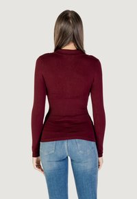 Maglione bordeaux a maniche lunghe con vita aderente a coste, texture liscia e scollatura a girocollo, abbinato a jeans fitted azzurri chiari.