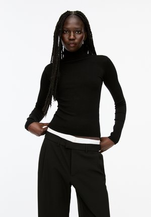 Black turtleneck sweater with a fitted design, long sleeves, and ribbed texture, paired with high-waisted black trousers featuring a white waistband.