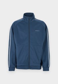 Σκούρο μπλε μπουφάν με φερμουάρ και ψηλό γιακά. Διαθέτει ανοιχτό γκρι ρίγες κατά μήκος των μανικιών, δύο μπροστινές τσέπες και ελαστικές μανσέτες.