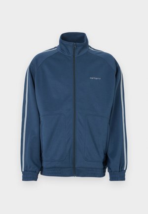 Σκούρο μπλε μπουφάν με φερμουάρ και ψηλό γιακά. Διαθέτει ανοιχτό γκρι ρίγες κατά μήκος των μανικιών, δύο μπροστινές τσέπες και ελαστικές μανσέτες.