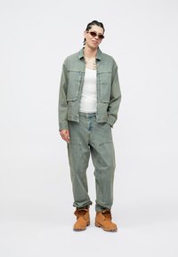 Φωτιστό μπλε τζιν μπουφάν με μεγάλες τσέπες, σε συνδυασμό με αντίστοιχο παντελόνι άνετης εφαρμογής. Το σύνολο ολοκληρώνουν καφέ αρβυλάκια με κορδόνια.