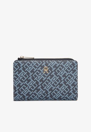 Portefeuille bleu marine avec motif géométrique bleu clair, matériau texturé, ferrures dorées et fermeture éclair. Détail du logo sur le devant.