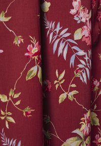 Tecido vermelho com padrão floral; apresenta flores cor-de-rosa, folhas verdes e detalhes azuis. Textura suave com um design fluido.