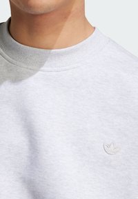 Felpa grigia chiaro con scollatura a coste e tessuto leggermente strutturato, caratterizzata da un piccolo logo bianco ricamato sul petto.