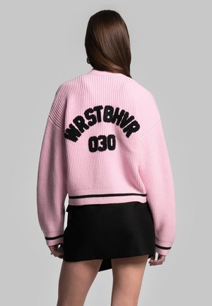 Rosa stickad bomberjacka med ribbad textur, med svart "WRSTBHVR 030" tryck på ryggen och svart randig nederkant.