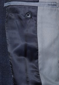 Skräddarsydda byxor med ett mörkt tyg på ena sidan och ett ljust randigt tyg på den andra, med en knappdetalj för knäppning.