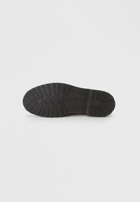 Suola di scarpa in gomma nera con motivo di battistrada testurizzato, caratterizzata da scanalature per trazione e stabilità. Design piatto, forma minimalista.