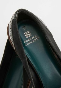 Scarpa slip-on in suede nera con soletta teal. Presenta un marchio in argento e cuciture a contrasto, creando un design elegante e moderno.