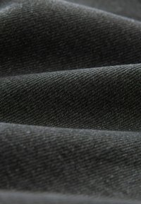 Mörkgrått tyg med en mjuk, strukturerad yta. Materialet har en liten lyster som framhäver diagonala vävmönster och vågiga veck.
