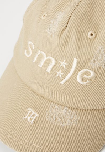 Beige cotton cap with embroidered text "sm*le" and a decorative accent. Features a curved visor and stitching details.