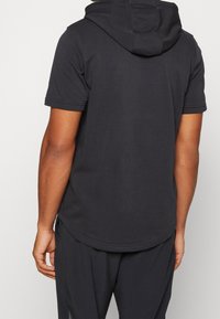 Musta, lyhythihainen huppari pyöreällä helmalla ja hupulla. Valmistettu pehmeästä kankaasta, yksivärinen malli, jossa ommellut saumat.