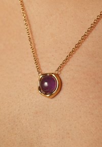 Gouden halsketting met een afgeronde paarse edelsteen hanger in een organic-vormige zetting, hangend aan een delicate ketting.