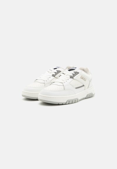 White leather sneakers with perforated toe, lace-up closure, padded collar, and grey accents. Rubber sole with textured tread pattern.