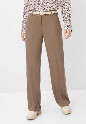Person iført beige vidde bukser, hvidt bælte, hvide fede sko og en langærmet mønstret bluse.