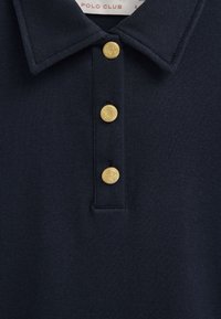 Dunkel marineblaues Poloshirt mit Kragen und drei dekorativen goldenen Knöpfen auf der vorderen Knopfleiste, strukturierter Stoff.