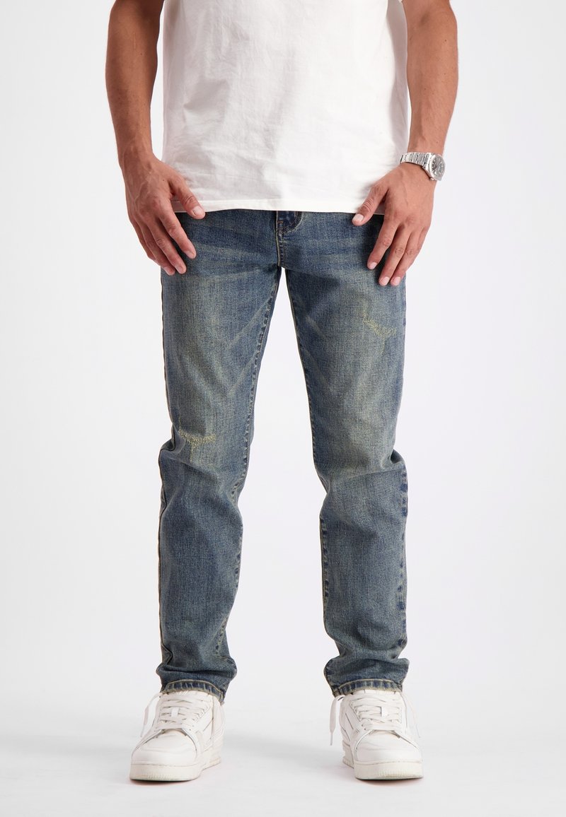 Vervaagde blauwe denim jeans met een rechte pasvorm, lichte slijtage en een vijf-vakkenontwerp, gedragen met witte sneakers.