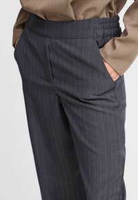 Gray pinstriped trousers with an elastic waistband and side pockets, featuring a smooth texture and subtle green accent stripes.
