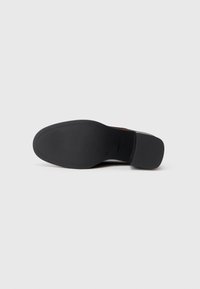 Suela de zapato negra con textura suave, forma contorneada y un logotipo estampado. Presenta un ligero tacón y un diseño limpio y minimalista.