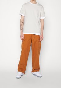 Ljusbeige bomullströja med vit kant, matchad med lösa orange cargobyxor. Vita sneakers med texturerad sula fulländar outfiten.