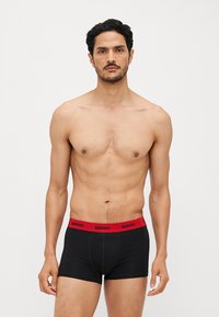 Schwarze Baumwoll-Boxershorts mit einem roten elastischen Bund, der das "DIESEL"-Logo trägt. Glatte Textur, enganliegendes Design und mittellange Beine.