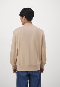 Maglione beige con scollo rotondo, maniche lunghe e vestibilità comoda, abbinato a jeans in denim blu. Tessuto liscio, design minimal.
