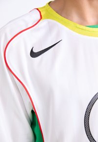 Hvid atletisk trøje med rund hals, der har grønne mesh sidedele, røde kanter og et sort Nike swoosh-logo på forsiden.
