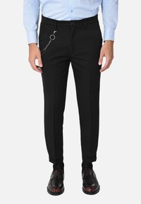 Pantaloni neri su misura con una vestibilità slim, caratterizzati da un accento con catena laterale, passanti per cintura e pieghe ordinate. Abbinati a scarpe eleganti lucide.