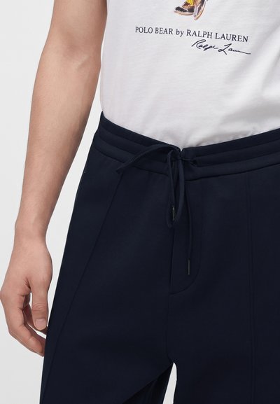 Бяла тениска с поло мече от Ralph Lauren, прибрана в тъмносини панталони с връзки, носена от човек с видимо ляво рамо и ръка.