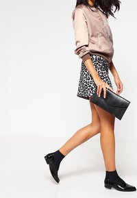 Vaaleanpunainen satiininen bomber-takki, musta leopardi-kuosisyksy, musta krokotiilinäköinen clutch-laukku, mustat sukat ja kiiltävät mustat loafer-kengät.