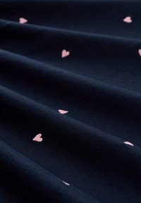 Ύφασμα σε ναυτικό μπλε με μικρά ροζ μοτίβα καρδιών διάσπαρτα και εμφανή πτυχώσεις που δημιουργούν απαλές σκιές.