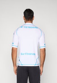 Camiseta deportiva blanca de manga corta con detalles y logotipos azules en la parte trasera. Presenta una textura suave y un diseño ajustado.