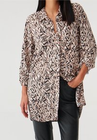 Camicia a maniche lunghe in tessuto leggero, con una base nera e un motivo floreale beige e pastello, chiusura a bottoni e vestibilità leggermente oversize.