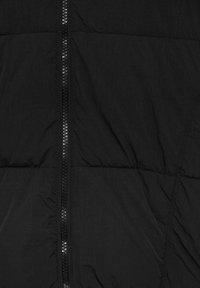 Tissu de veste matelassée noire avec une grande fermeture éclair verticale au centre, coutures détaillées sur les côtés.
